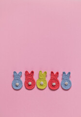 Cute colorful crochet bunnies with white tails on a pink background. Happy Easter concept. Top view. Copy space.