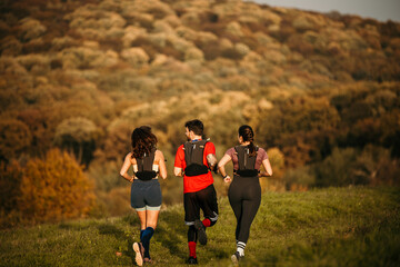 Rear view of a diverse group of young people exercising outdoors, preparing for a mountain trail. They are wearing sports clothing and a trail running vest