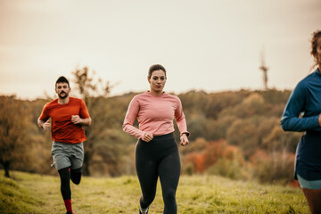 Two women and a man running on a trail in a mountain area, focus on their faces as they enjoy the exercise. Depicting trail running, healthy lifestyle, friendship, and exercise in the great outdoors