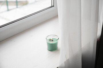 Candle burning on home window sill, too close to the curtain creating fire hazard. Conceptual image.