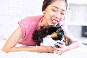 Young beautiful cat lover working woman with cute cat lying in bed at home and having fun on bed