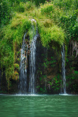View of scenic amazing waterfall in national park in summer - moving flowing water, hanging plants and vivid emerald pond - fresh coolness on a hot tropical day, attraction for tourism and travel