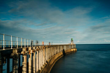 Whitby Harbour pier with lighthouse and wooden boards with metal railings and the sea in the background.