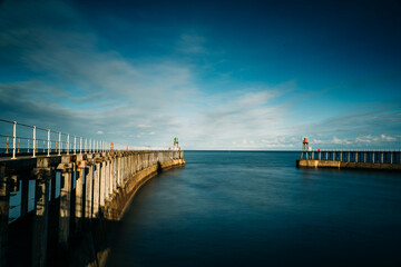 Fototapeta premium Whitby Harbour pier with lighthouse and wooden boards with metal railings and the sea in the background.