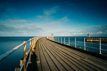 Obraz premium Whitby Harbour pier with lighthouse and wooden boards with metal railings and the sea in the background.