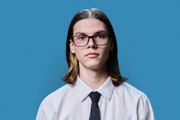 Headshot portrait of serious teenage guy on blue studio background