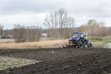 Tractor plows black earth in garden, autumn rural view