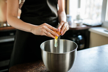 someone breaks an egg into a mixing bowl
