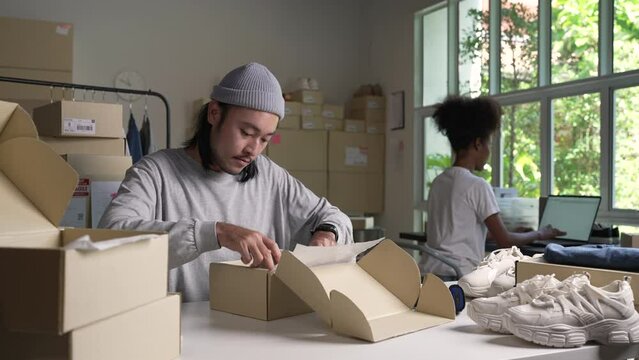 Mixed race couple of Asian man and African-American woman online seller e-commerce business owner working together in store warehouse.