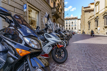 Obraz na płótnie Canvas Scooters and motorcycles parked in a perfect row on a street in Italy