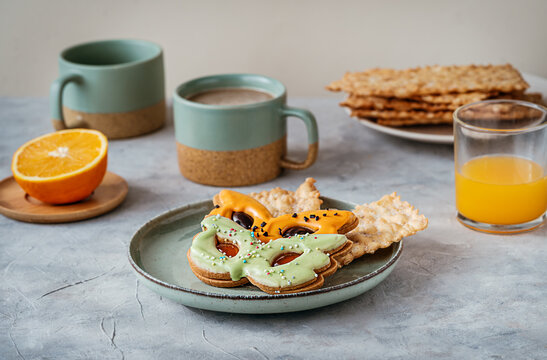 Carnival sweets in shape of carnival mask green and orange colour, cacao in mugs, orange fruit, carnival fritters or bugie on light grey background