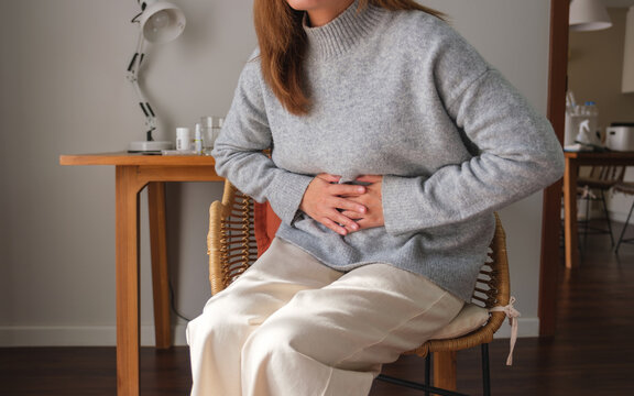 Closeup Image Of A Sick Woman Suffering From Stomachache, Abdominal Pain While Sitting On Sofa At Home