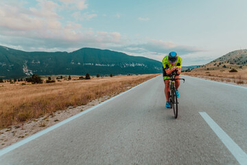 Fototapeta premium Full length portrait of an active triathlete in sportswear and with a protective helmet riding a bicycle. Selective focus 