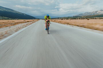 Fototapeta premium Full length portrait of an active triathlete in sportswear and with a protective helmet riding a bicycle. Selective focus 