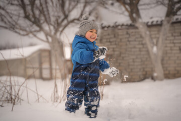 Funny little boy in blue winter clothes walks during a snowfall. Outdoors winter activities for...
