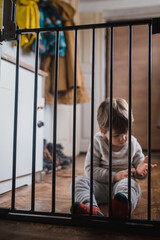 Toddler tries open lock on child safety gate. The child plays behind the security gate in front of the stairs at home. Front view of a little boy standing on the other side of the child safety