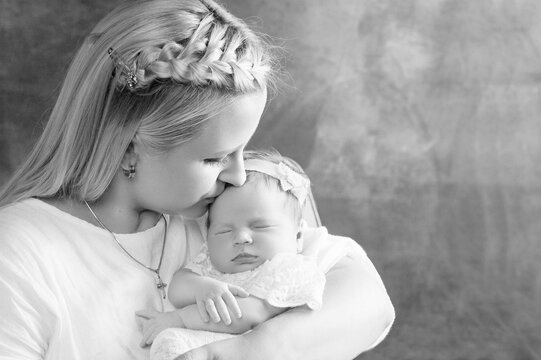 Pretty woman holding a newborn baby girl in her arms. Happy mother kissing her slipping newborn baby.  Happy family concept. Close up picture.