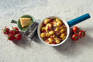 Pan with delectable gnocchi on table with cheese and tomatoes
