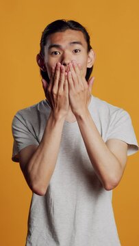 Vertical video: Asian adult sending air kisses on camera, acting funny and romantic in studio. Young carefree person blowing kisses and being flirty, acting sensual with kissy silly face. Natural