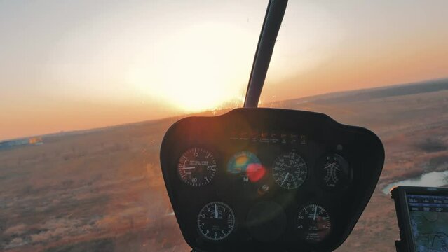 View from the inside of a helicopter through windshield while flying on low altitude. Cockpit dashboard against soft sunset