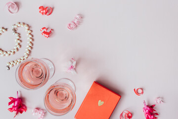 top view, close-up, table decoration on a pink background for valentine's day, two red croissants, a red box with a gift, two glasses of rose wine or champagne, a pearl necklace
