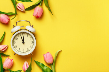 Alarm clock surrounded by tulips. Transitional change of time, change of seasons. copy space