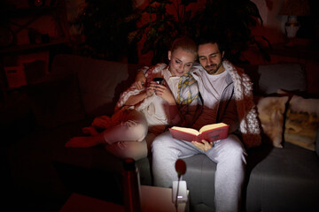 Lovely couple. Cozy evening. Man and woman in warm blanket sitting on sofa, hugging and reading...
