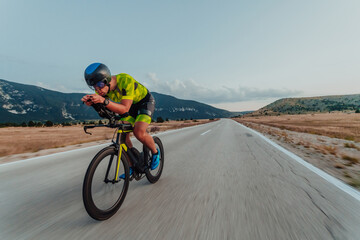 Naklejka premium Full length portrait of an active triathlete in sportswear and with a protective helmet riding a bicycle. Selective focus 