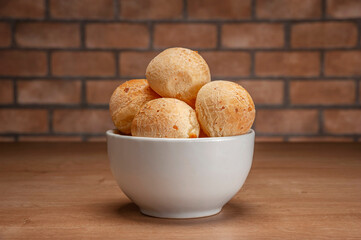 Cheese breads in a white bowl on wooden table and bricks wall background.