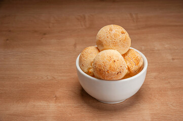 Cheese breads in a white bowl on wooden table.