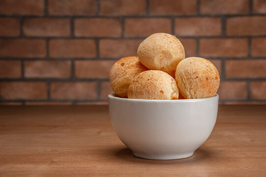 Cheese breads in a white bowl on wooden table and bricks wall background.