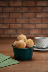 Cheese breads in a green ramekin with a cup of coffee on wooden table and bricks wall background.