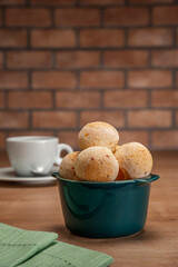 Cheese breads in a green ramekin with a cup of coffee on wooden table and bricks wall background.