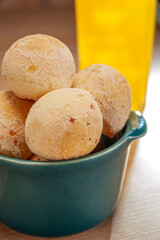 Cheese breads in a green ramekin with a glass of orange juice on wooden table and bricks wall background.