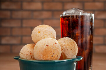 Cheese breads in a green ramekin with a glass of cola soft drink on wooden table and bricks wall background.