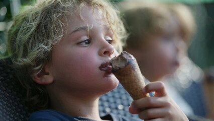 One pensive child eating chocolate ice cream cone outside. Blonde young boy eats sweet dessert