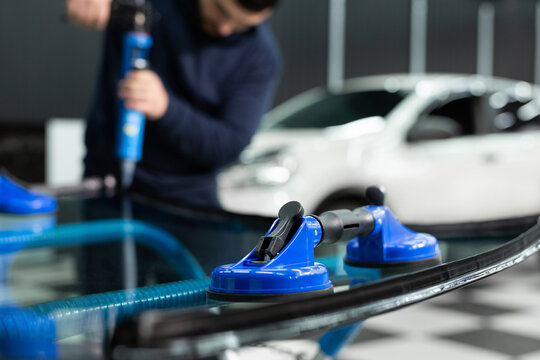 An experienced man in work clothes applies a black sealant to the glass before installing it on the car.