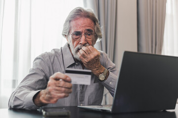 Upset senior elderly man holding credit card by laptop having trouble worry finance safety data or...