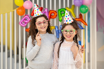 Two cute girls pose against a bright wall with balloons at a children's birthday party. © Studio Peace