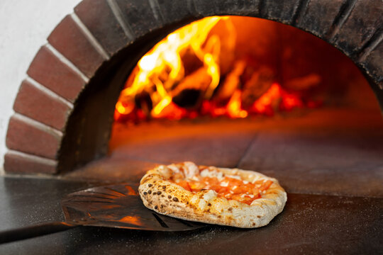 Italian pizza is cooked in a wood-burning oven. The cook puts the pizza in the oven on a shovel.