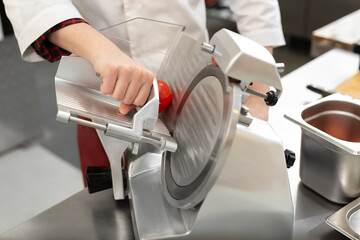 The chef in the restaurant kitchen prepares tomato slices with a slicer.