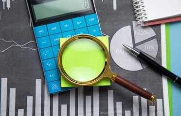 Magnifying glass with a sticky note on financial graphs.
