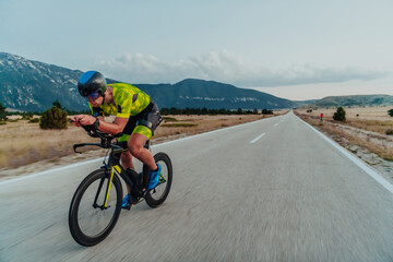 Full length portrait of an active triathlete in sportswear and with a protective helmet riding a bicycle. Selective focus  - obrazy, fototapety, plakaty