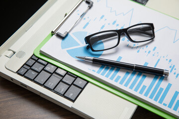 Pen, eyeglasses, graphs on the computer keyboard.