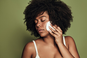 Tranquil young black woman applying toner on face with cotton pad © kegfire