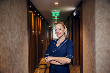 A confident chambermaid standing in a hotel lobby with arms crossed.