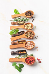 Various spices and green herbs in wooden spoons on white table
