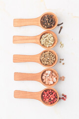 Various spices and green herbs in wooden spoons on white table