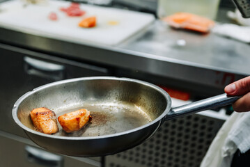 man chef cooking fried salmon fish in frying pan on kitchen