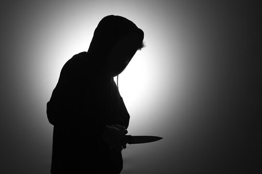 Mysterious man wearing black hoodie holding a knife to stab someone. Crimes and criminality concept